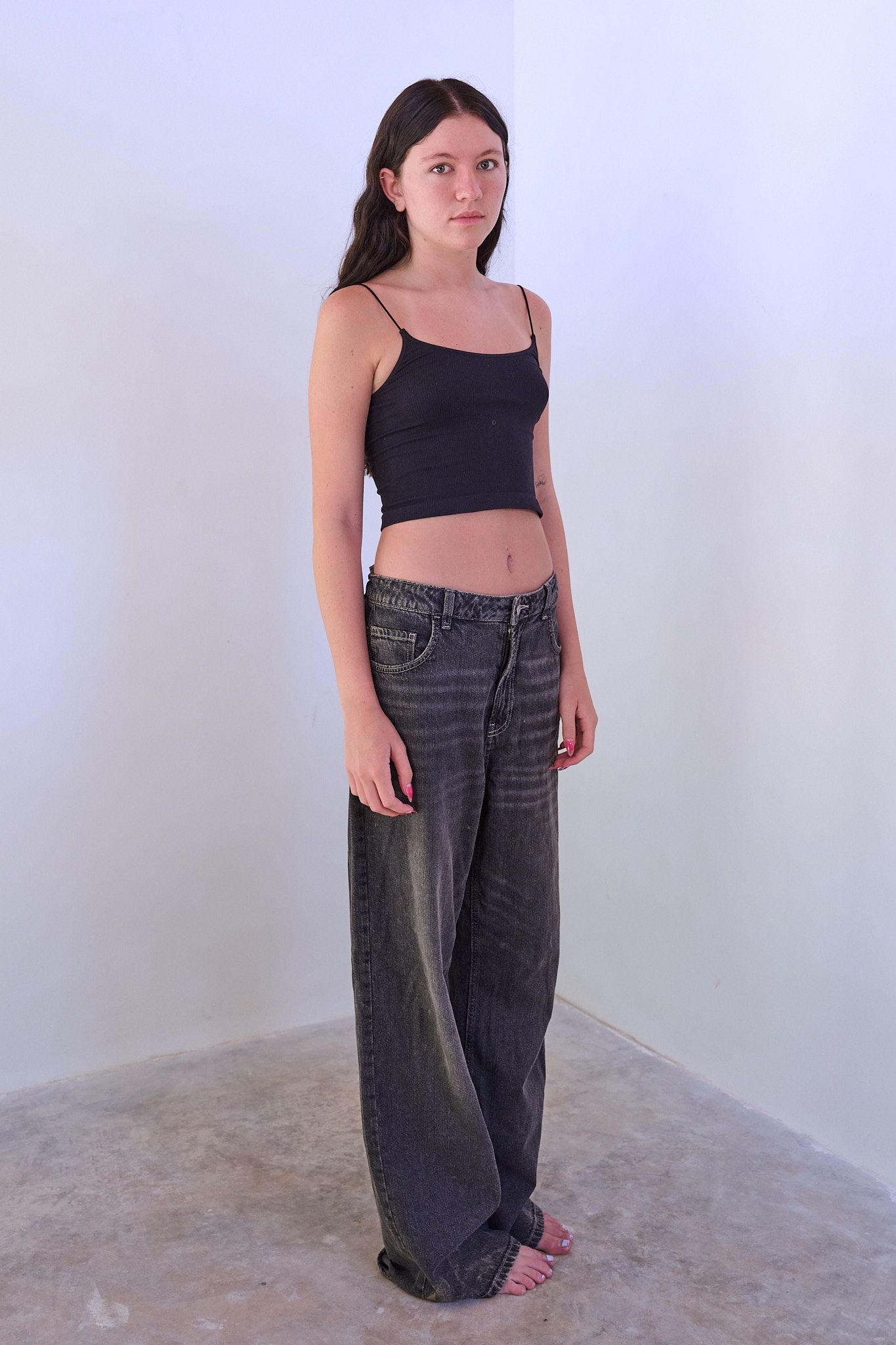 Model in white crop top and baggy blue jeans poses on black stool against light background.