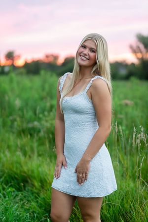 A person in a white lace dress poses in a lush green field at sunset.