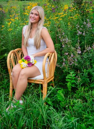 A person in a white dress sits on a wooden chair surrounded by vibrant wildflowers and lush summer garden foliage.
