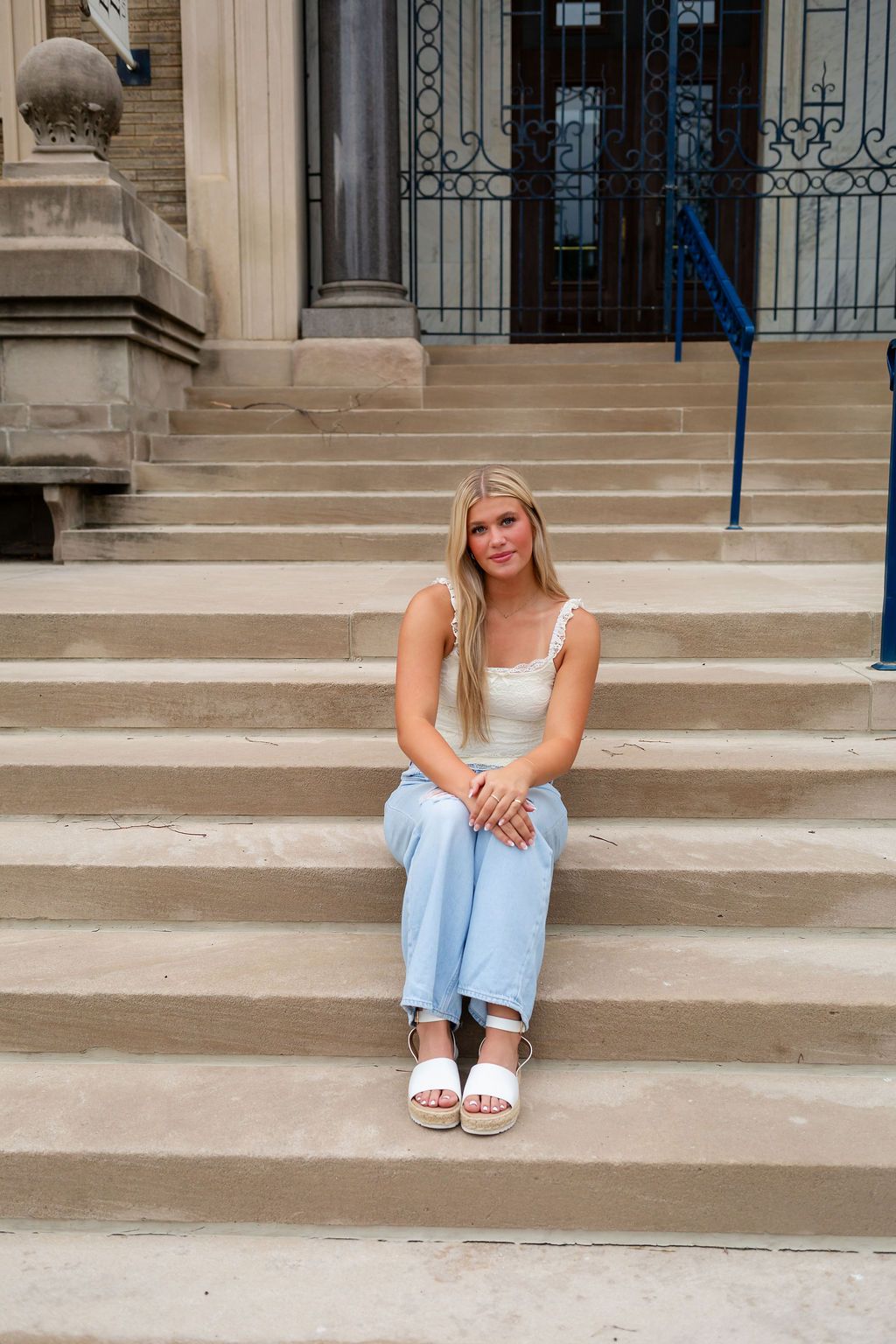 Outdoor photo session on stone steps with light denim jeans and white sandals.
