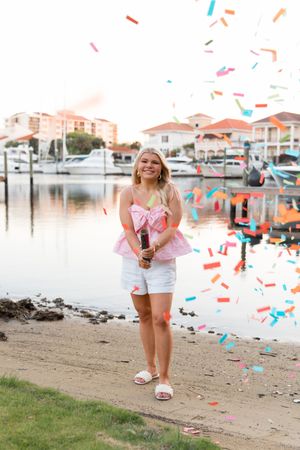 Colorful confetti falls around a marina with boats and waterfront homes in the background on a sunny day.