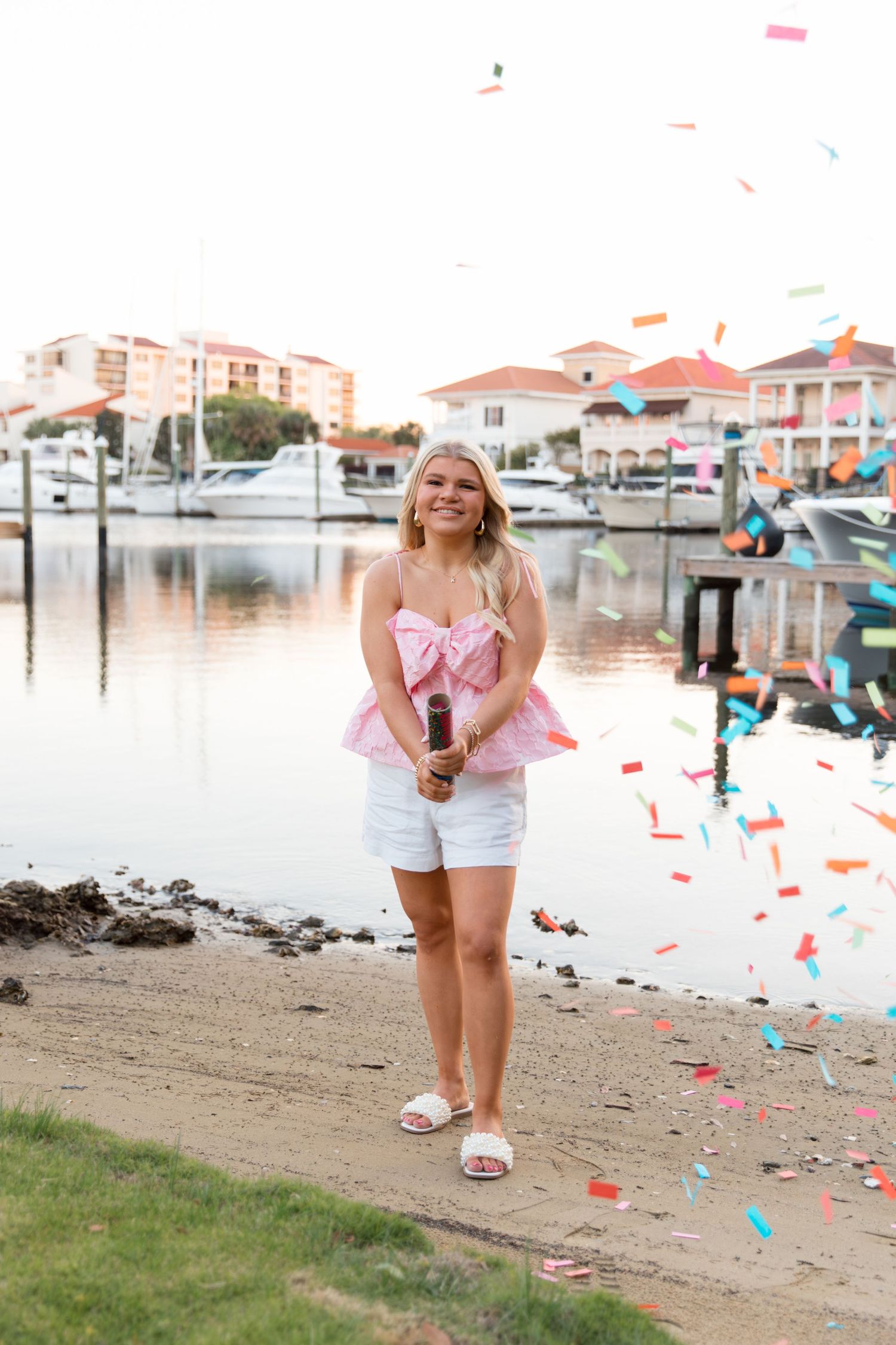 Colorful confetti falls on a sandy beach near a marina with boats and buildings in the background.