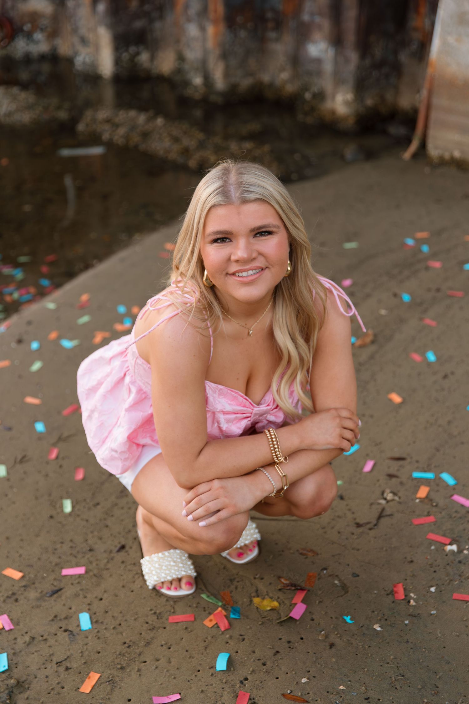 A person in a pink dress poses playfully with colorful confetti scattered on the ground.