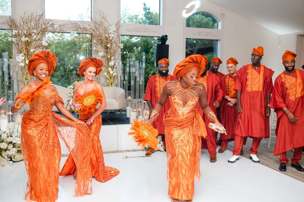 Group wearing bright orange traditional attire walking in procession during cultural celebration.