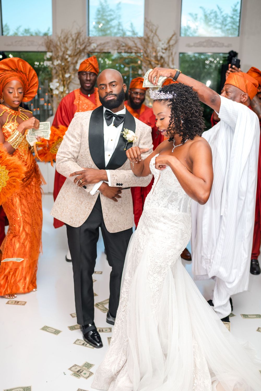 Wedding party dances and celebrates in formal attire with vibrant orange and white decorations at an elegant reception.