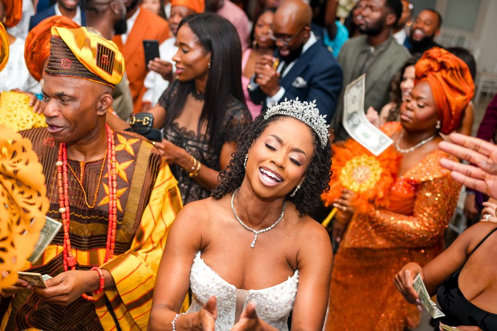 Wedding guests dance and celebrate joyfully at a vibrant reception with orange and gold decor.