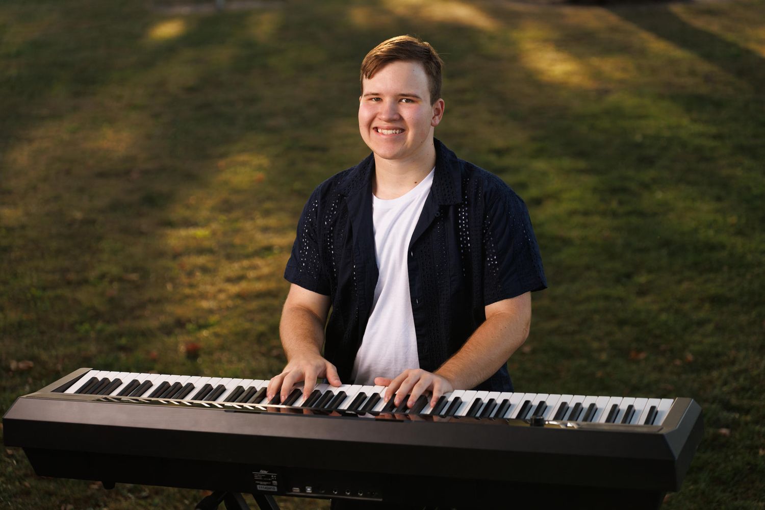 Musician performs on digital keyboard piano outdoors in natural lighting during golden hour.