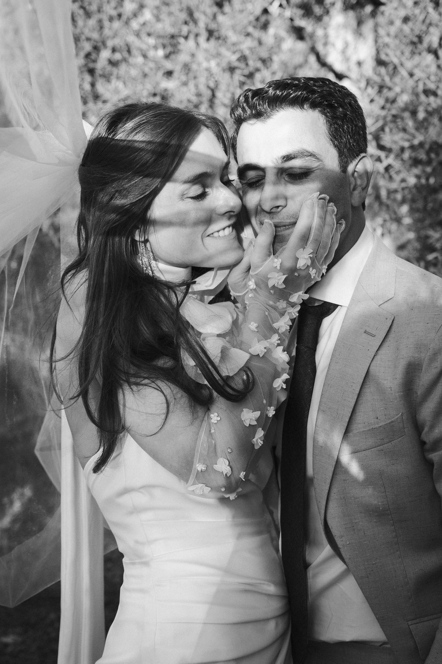 Black and white photo sequence of a romantic kiss between newlyweds under a flowing veil at an outdoor wedding ceremony.