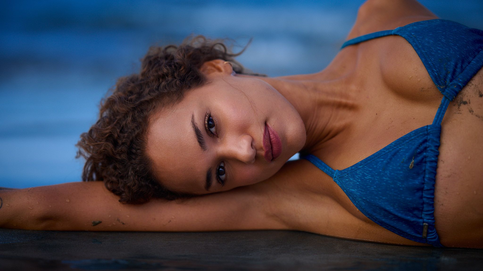 A person wearing blue loungewear rests on a surface in a series of artistic poses against a blue background.
