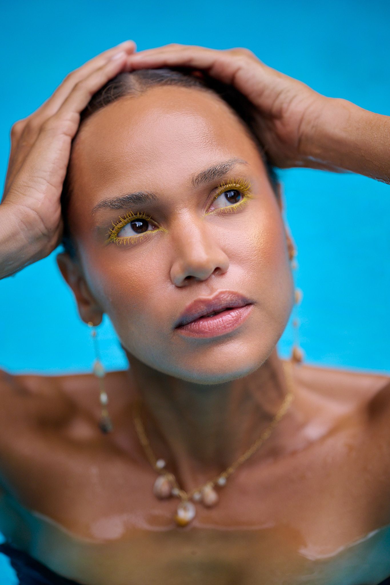 Artistic beauty portrait against vibrant blue background with dramatic lighting and gold eye makeup details.