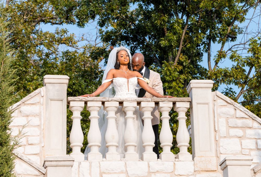 A couple poses along an ornate white stone balustrade in an elegant outdoor wedding setting.