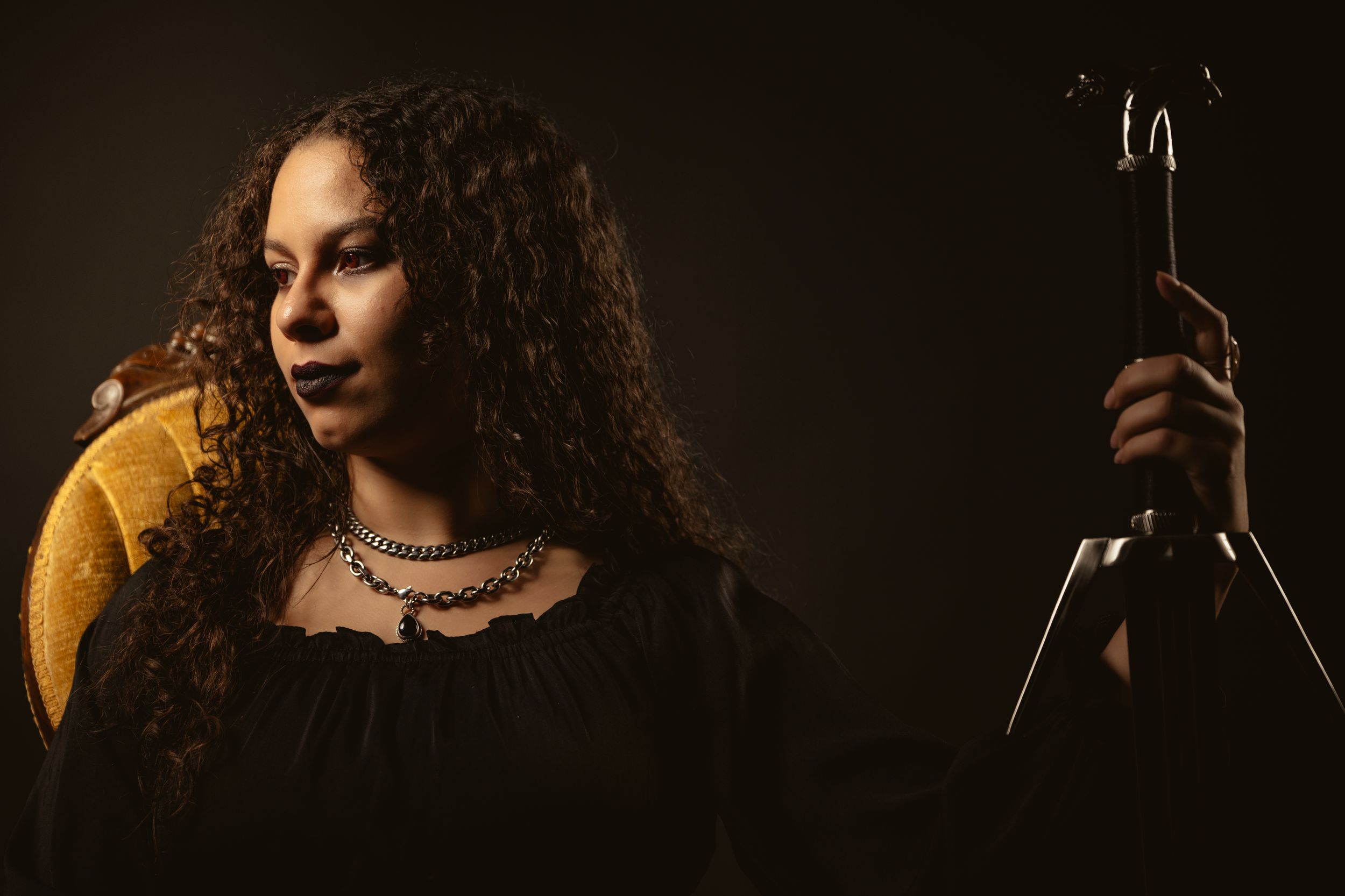A person with curly hair performs on stage under dramatic lighting against a dark background.