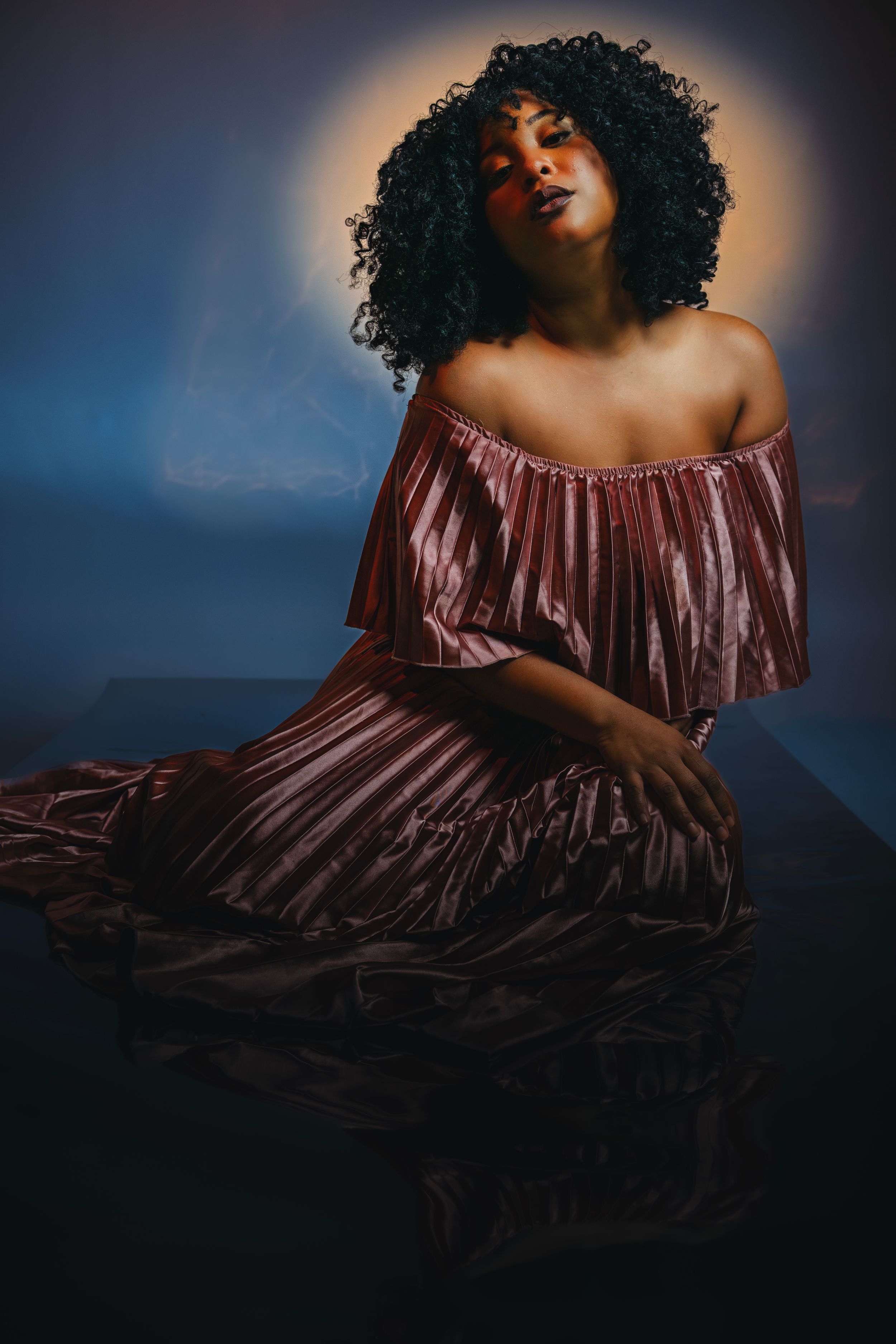 A figure in a flowing burgundy velvet dress poses dramatically against a dark moody background in an artistic portrait series.