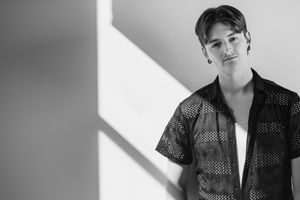 Black and white portrait of someone wearing a patterned shirt against a wall with angular shadows.