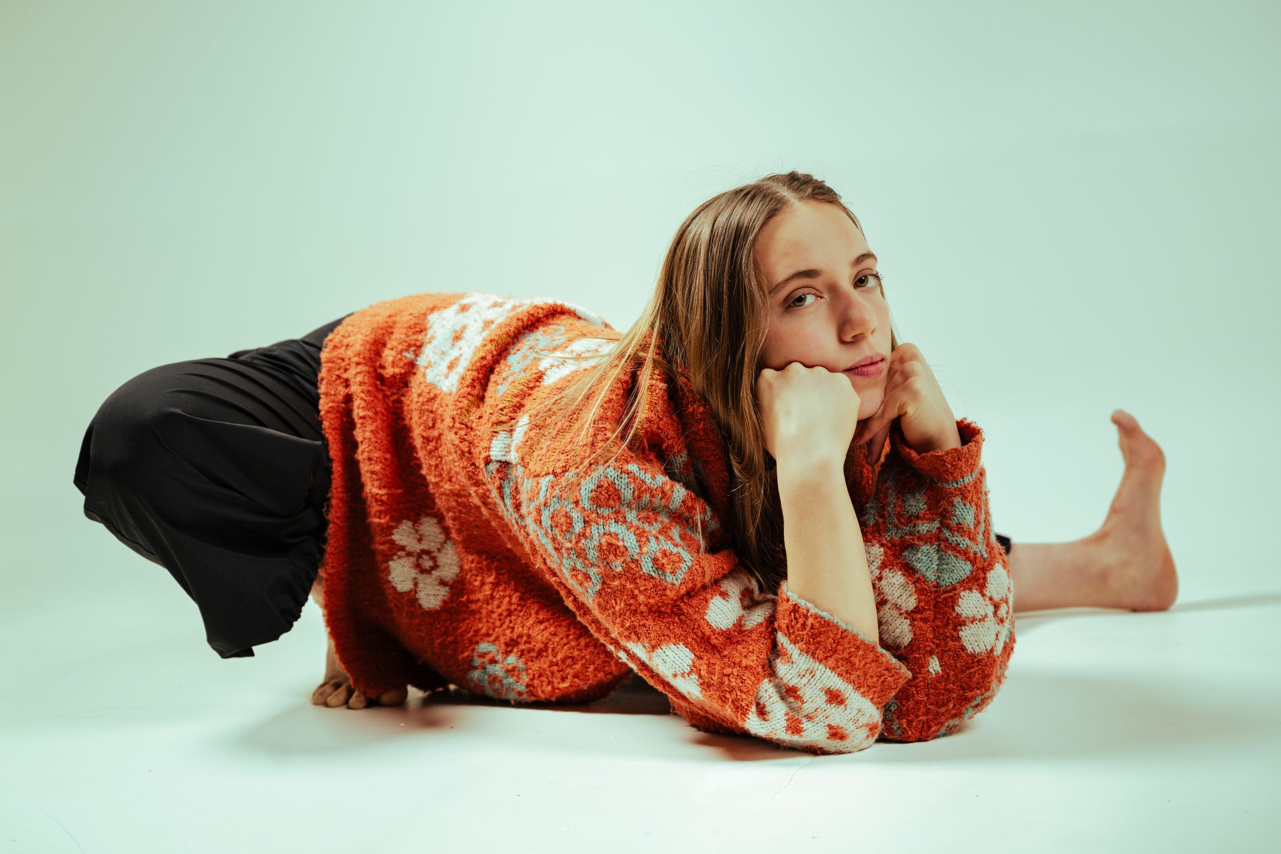 A person in an orange floral dress performs a graceful dance sequence across a white studio floor.