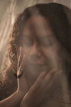 A soft, ethereal portrait in sepia tones showing a person with curly hair and closed eyes in a dreamy pose.