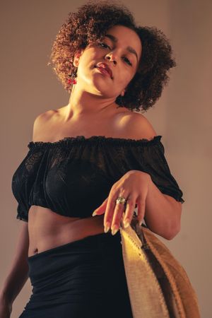 Artistic fashion portrait in warm lighting shows model in black top posing expressively against neutral backdrop.