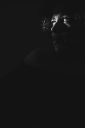 A dark, dramatic silhouette of a person stands against a black background creating a moody artistic portrait.