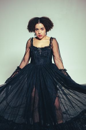 A flowing black tulle dress with sheer layers is modeled against a light gray studio backdrop.