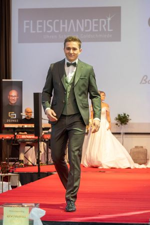 Men in green formal suits walk the runway at a wedding fashion show.