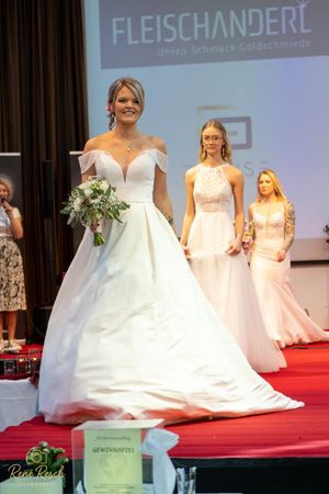 Multiple wedding gowns displayed simultaneously on red carpet during bridal fashion event.