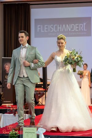 Wedding fashion show featuring formal suits and gowns on a red carpeted stage with professional lighting.