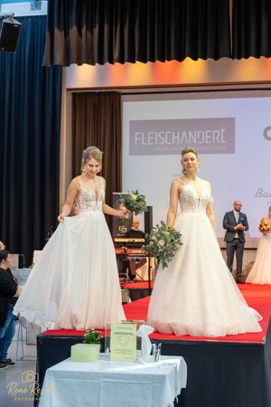 Bridal fashion show featuring white wedding gowns displayed on an illuminated red carpet runway.
