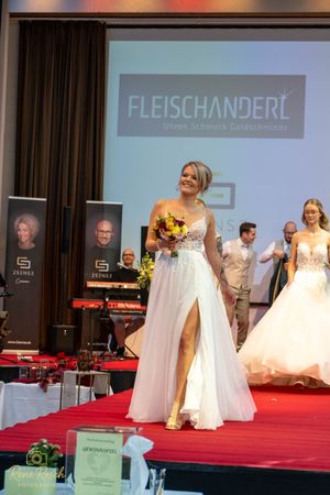 Multiple wedding dresses on display during a bridal fashion show with stage lighting.