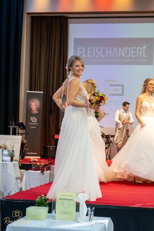 Bridal fashion showcase featuring white wedding gowns on a red carpet runway with display tables.