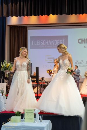 Bridal fashion event showcasing multiple white wedding dresses on an elevated runway stage.