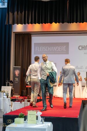 Models walking down a red carpet runway at a fashion show featuring Fleischanderl designs.