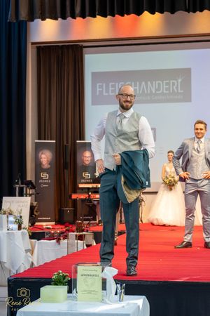 A model in business attire walks confidently down the red carpet during a Fleischanderl fashion show.