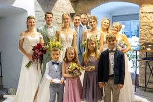Wedding party poses together in formal attire under stone archways.