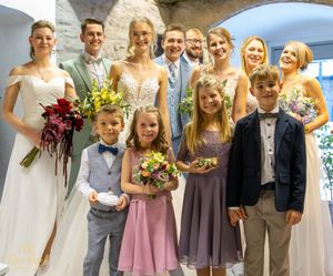 Wedding party members pose together in coordinated formal attire under an archway.
