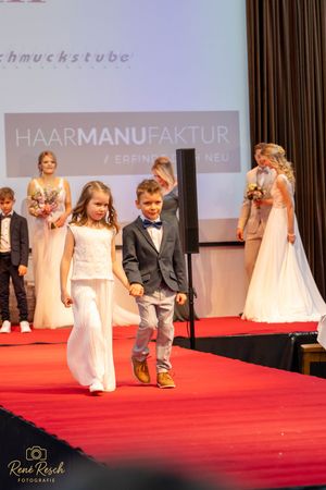 Wedding fashion show participants walking down a red carpet runway with studio lighting.