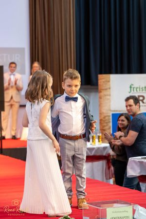 Children's formal wear fashion show with young models on a bright red runway.