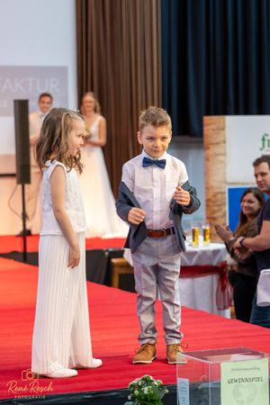 Young models showcase formal attire while walking a red carpet runway at a fashion event.