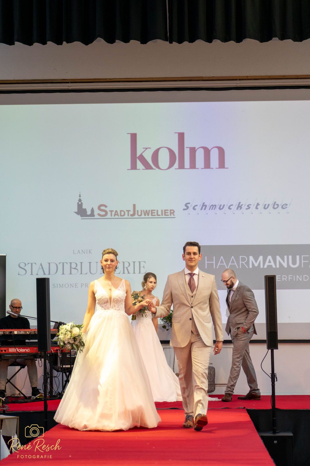 Bridal fashion show on red carpet runway featuring elegant white gowns and tan suits.