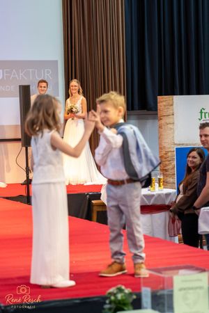 Fashion show featuring young models in formal wear walking down a red carpet runway.