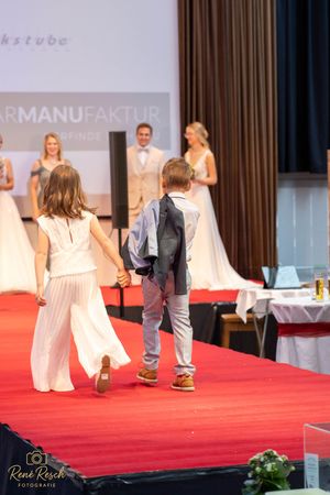 Models showcase wedding and formal attire on a red carpet runway with stage lighting.