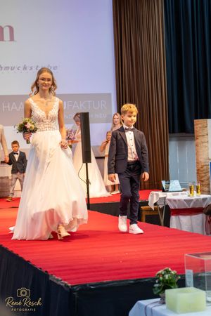 Models showcase elegant wedding attire while walking down a red carpet runway at a bridal fashion show.