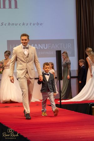 A pair of models walk the runway in formal wear during a fashion show event.