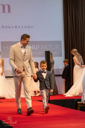 Models showcase formal attire while walking together on a red carpet runway.