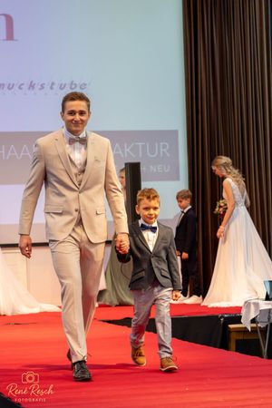 Two models walk hand in hand down a red carpet runway at a formal fashion event.