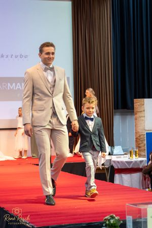 Models display elegant suits while walking a fashion runway together.