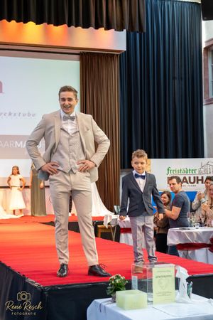 Models pose in formal attire on a red carpet runway during a fashion event.