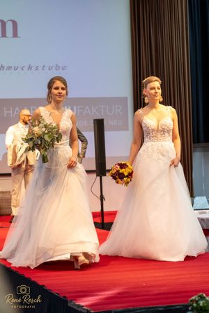 Bridal fashion show finale with models in white wedding dresses carrying floral bouquets.