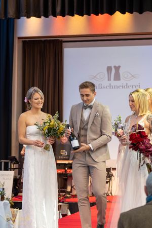 Bridal fashion show featuring models in white wedding dresses and formal attire on red carpet runway.