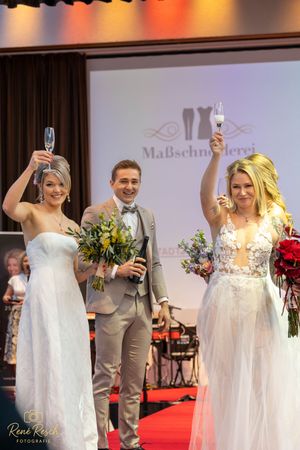 Wedding fashion show models holding bouquets and raising champagne glasses on red carpet.