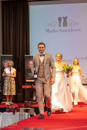 Wedding fashion show featuring formal wear and bridal gowns with logo backdrop on stage.
